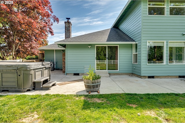 back of property featuring a hot tub, a patio area, a lawn, and a chimney