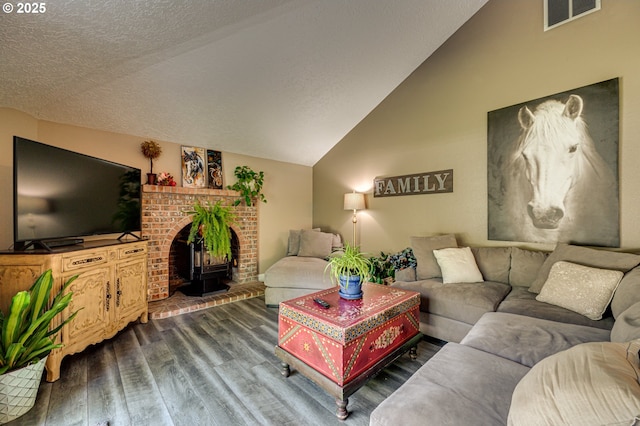 living room with wood finished floors, lofted ceiling, a wood stove, and a textured ceiling