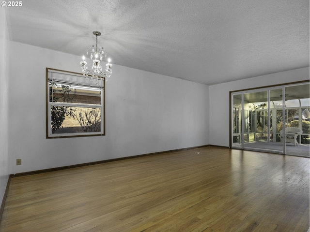 unfurnished room featuring hardwood / wood-style floors, an inviting chandelier, and a textured ceiling