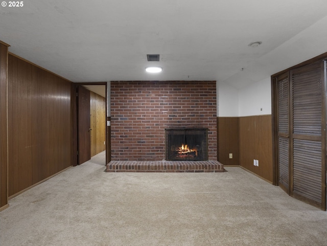 unfurnished living room featuring light colored carpet, wooden walls, and a brick fireplace