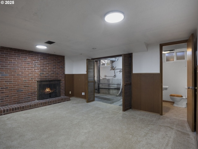 basement with wood walls, light colored carpet, and a brick fireplace