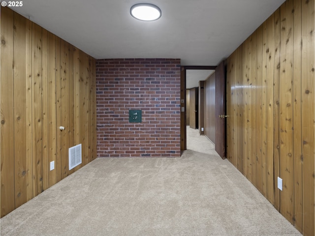 unfurnished room featuring brick wall, light carpet, and wooden walls