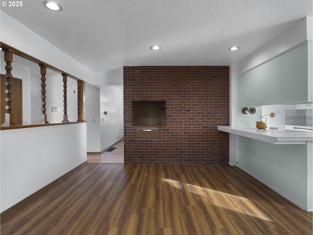 unfurnished living room featuring brick wall, a textured ceiling, and dark hardwood / wood-style flooring