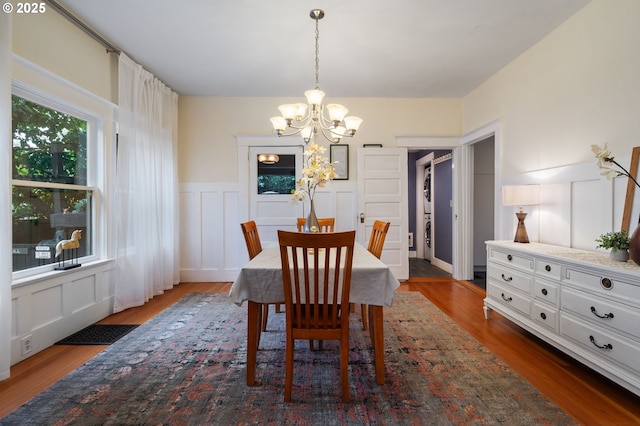 dining room with a chandelier, a decorative wall, dark wood finished floors, and wainscoting