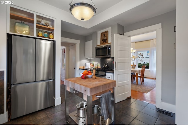 kitchen featuring visible vents, dark countertops, appliances with stainless steel finishes, dark tile patterned floors, and open shelves