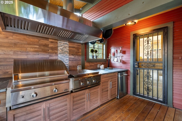 kitchen with brown cabinetry, wood finished floors, wood walls, and exhaust hood