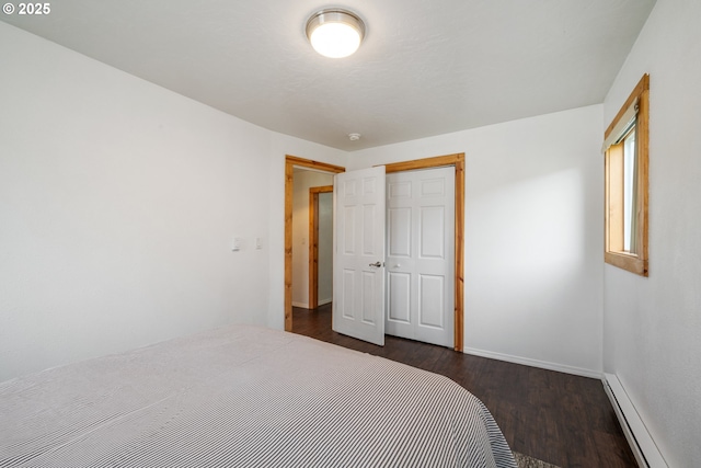 bedroom featuring a baseboard radiator, baseboards, a closet, and dark wood finished floors