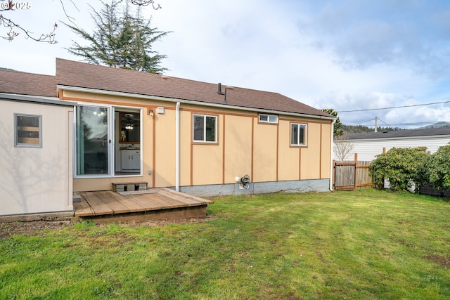 back of house featuring a wooden deck, a lawn, roof with shingles, and fence