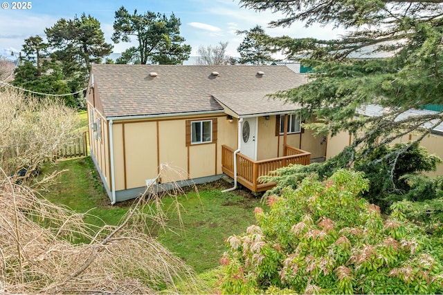 rear view of property with a lawn, roof with shingles, and fence