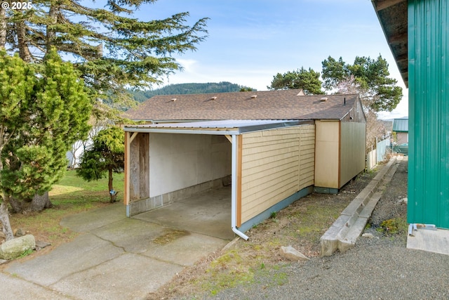 view of side of property featuring a detached garage and roof with shingles