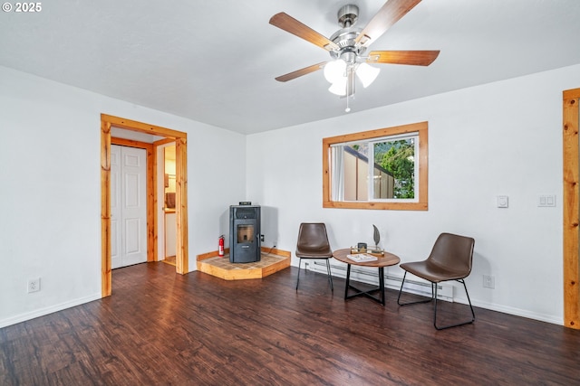 sitting room featuring ceiling fan, baseboards, a wood stove, wood finished floors, and a baseboard radiator