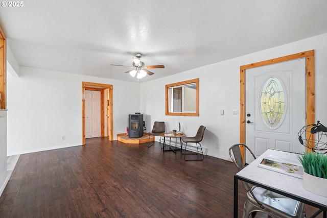 foyer with dark wood-type flooring, a wood stove, a ceiling fan, and baseboards