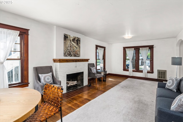 living room featuring wood finished floors, a brick fireplace, and baseboards