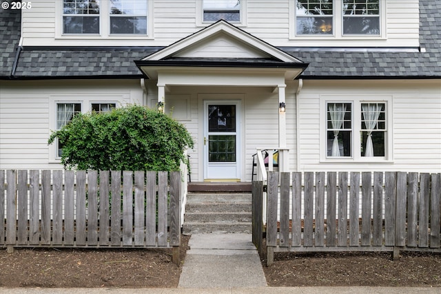 view of exterior entry with roof with shingles and fence