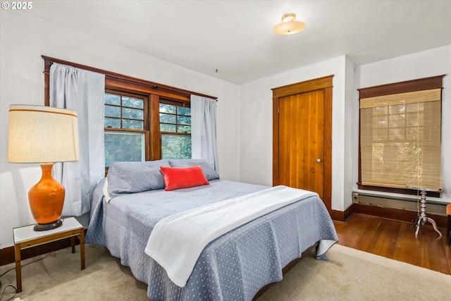 bedroom featuring a closet, baseboard heating, wood finished floors, and baseboards