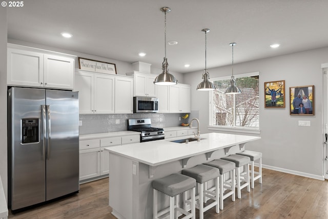 kitchen with an island with sink, light countertops, decorative backsplash, stainless steel appliances, and a sink