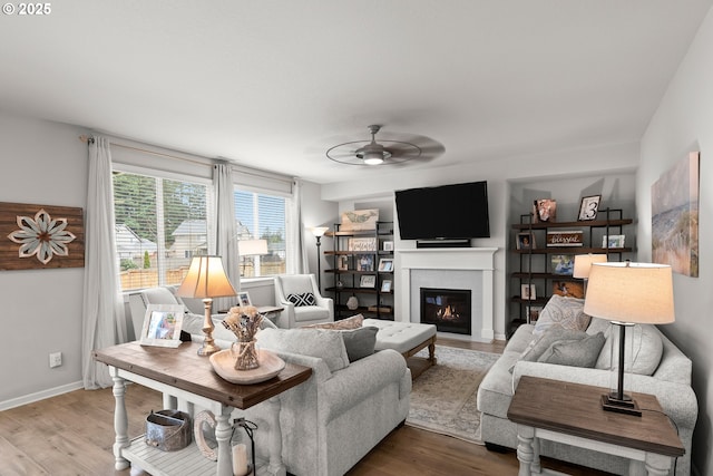 living room featuring a glass covered fireplace, baseboards, ceiling fan, and wood finished floors