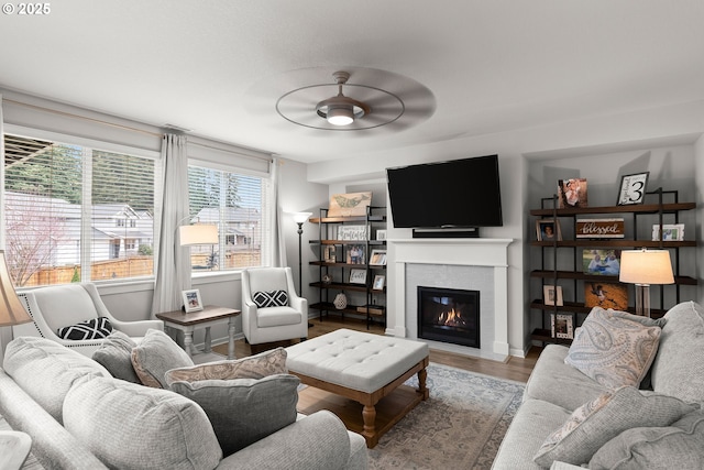 living area featuring baseboards, a fireplace with flush hearth, wood finished floors, and a ceiling fan