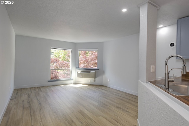 unfurnished living room featuring cooling unit, a sink, baseboards, and light wood-type flooring