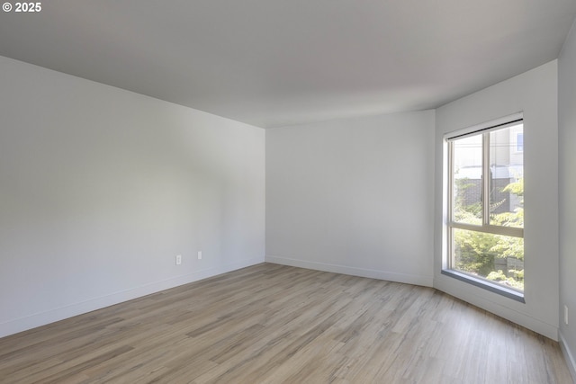 empty room featuring light wood finished floors, a wealth of natural light, and baseboards