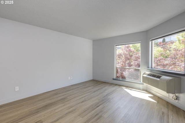 spare room featuring baseboards, cooling unit, light wood-style floors, and plenty of natural light