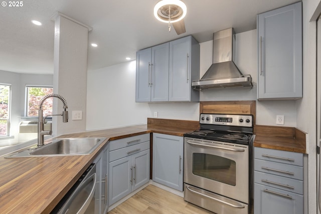 kitchen featuring wood counters, wall chimney range hood, a sink, appliances with stainless steel finishes, and gray cabinetry