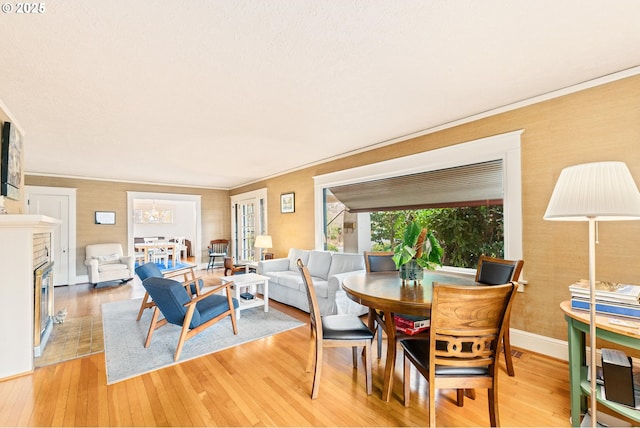 dining room with light wood finished floors, a glass covered fireplace, baseboards, and ornamental molding