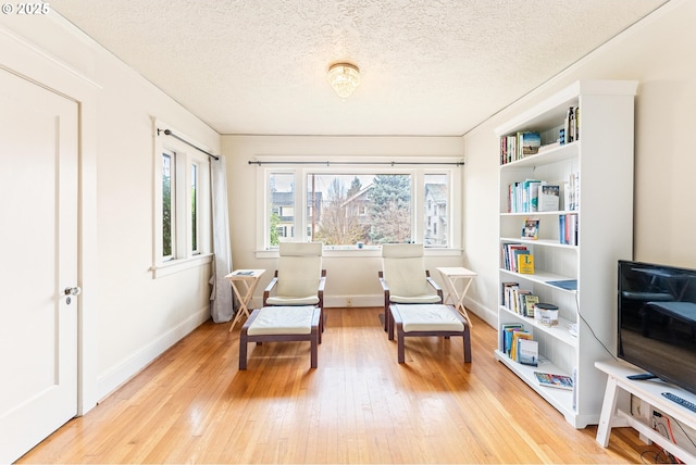 sitting room with baseboards, light wood-style floors, and a textured ceiling