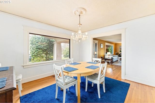 dining room with ornamental molding, light wood-style floors, baseboards, and a chandelier