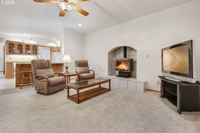 carpeted living room featuring vaulted ceiling, a wood stove, and ceiling fan