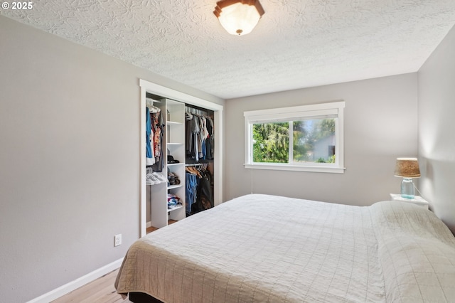 bedroom featuring wood finished floors, baseboards, a closet, and a textured ceiling