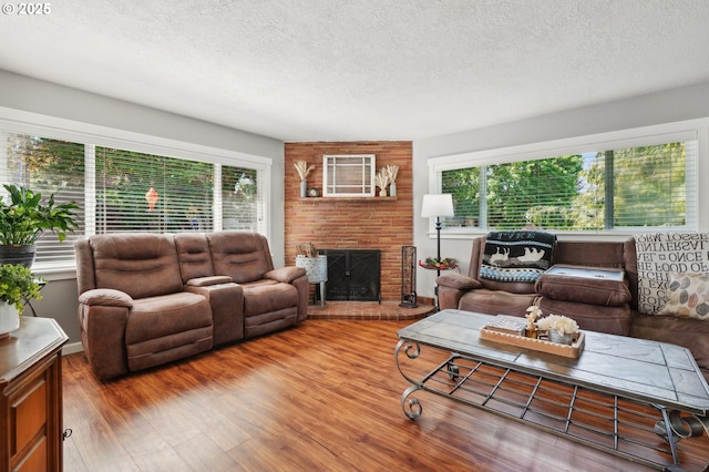 living area featuring a textured ceiling, plenty of natural light, a brick fireplace, and wood finished floors
