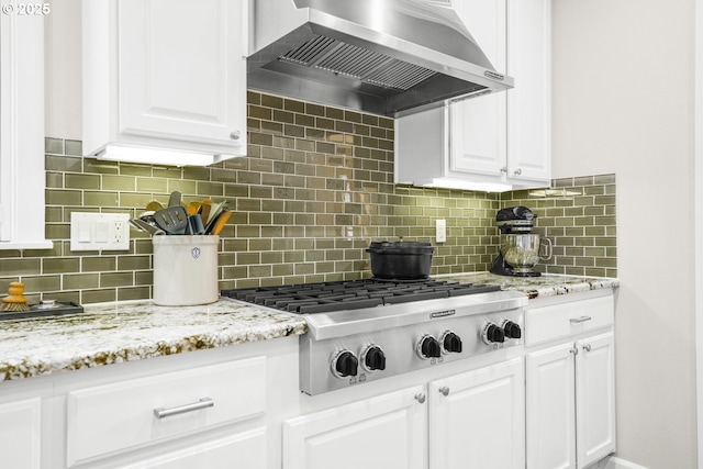 kitchen with wall chimney range hood, light stone countertops, white cabinetry, and stainless steel gas stovetop