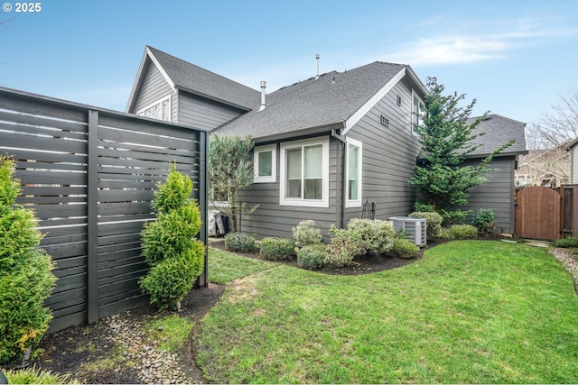 rear view of property featuring a lawn, roof with shingles, a gate, fence, and central AC