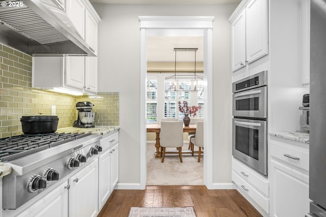 kitchen featuring wall chimney range hood, appliances with stainless steel finishes, white cabinets, and dark wood-type flooring