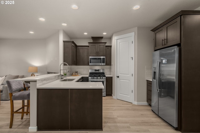 kitchen with appliances with stainless steel finishes, open floor plan, a peninsula, light countertops, and a sink