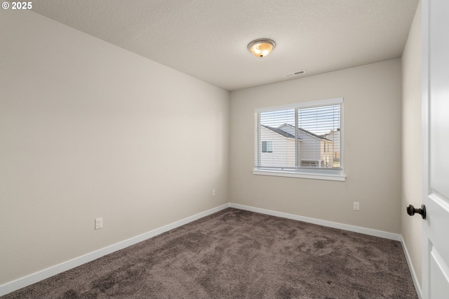 spare room featuring dark colored carpet, visible vents, a textured ceiling, and baseboards