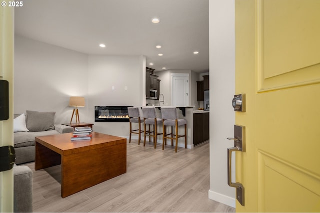 living area featuring light wood-type flooring, a glass covered fireplace, and recessed lighting