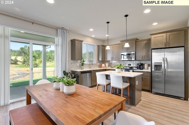 kitchen with appliances with stainless steel finishes, a center island, light wood-type flooring, hanging light fixtures, and sink