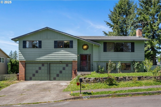 bi-level home featuring a chimney, an attached garage, driveway, and brick siding