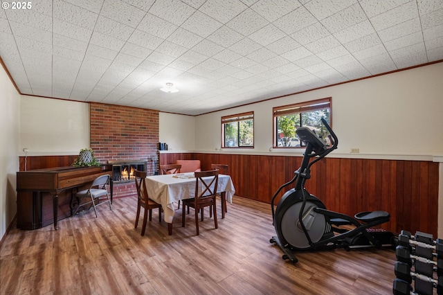 dining area featuring a wainscoted wall, a brick fireplace, wood finished floors, ornamental molding, and wooden walls