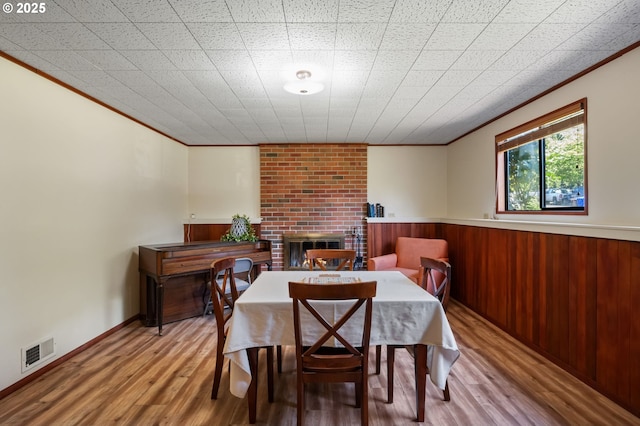 dining room with a fireplace, ornamental molding, wood finished floors, and wooden walls