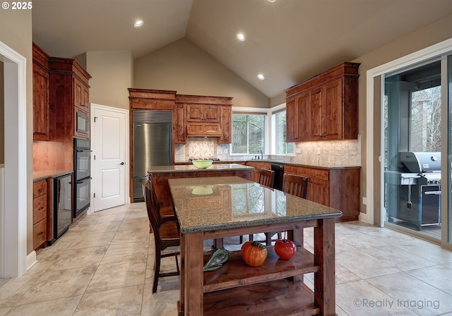 kitchen with sink, light stone counters, tasteful backsplash, a kitchen island, and black appliances