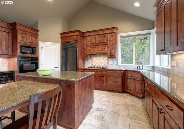 kitchen with sink, dark stone countertops, a center island, black appliances, and a kitchen bar