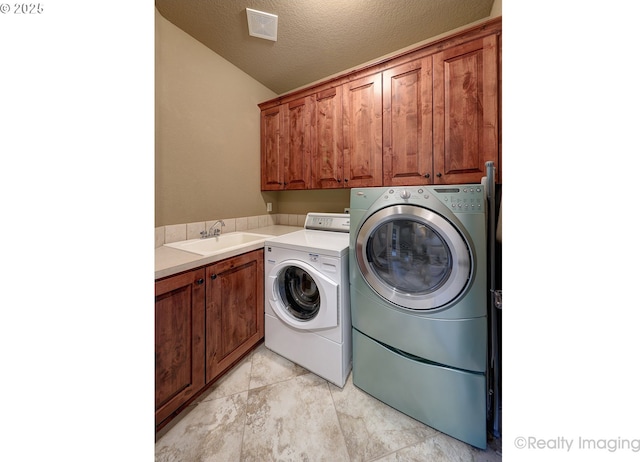 clothes washing area with sink, cabinets, light tile patterned floors, washing machine and clothes dryer, and a textured ceiling