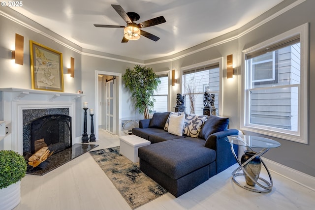 living room featuring crown molding, light hardwood / wood-style flooring, a premium fireplace, and ceiling fan