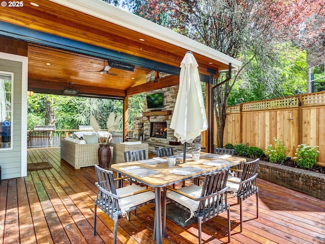 deck with ceiling fan, fence, outdoor dining space, and an outdoor living space with a fireplace