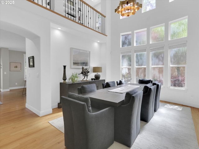 living area featuring a towering ceiling, arched walkways, light wood-type flooring, baseboards, and a chandelier
