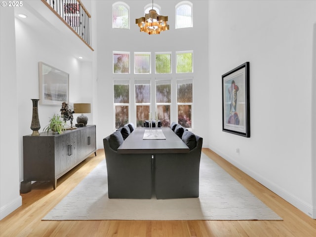 dining area with baseboards, a high ceiling, light wood-style flooring, and a chandelier
