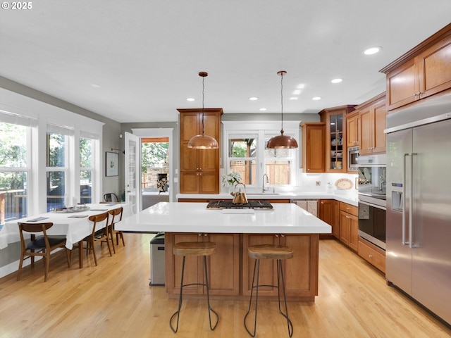 kitchen featuring glass insert cabinets, built in appliances, brown cabinetry, and a center island